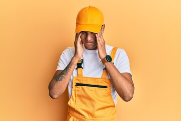 Poster - Young handsome african american man wearing handyman uniform over yellow background with hand on head, headache because stress. suffering migraine.