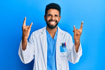 Sticker - Handsome hispanic man with beard wearing doctor uniform shouting with crazy expression doing rock symbol with hands up. music star. heavy concept.