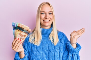 Poster - Young blonde girl holding canadian dollars smiling cheerful presenting and pointing with palm of hand looking at the camera.