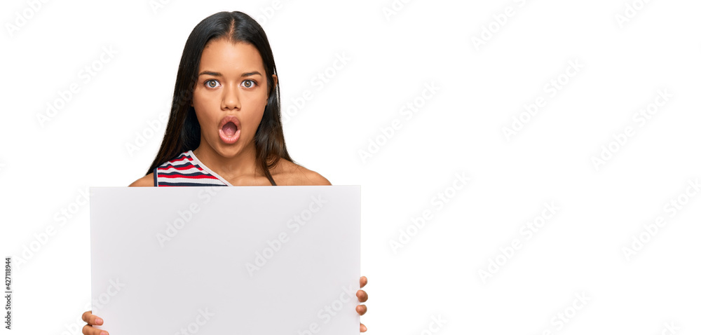 Beautiful hispanic woman holding blank empty banner scared and amazed with open mouth for surprise, disbelief face - obrazy, fototapety, plakaty 