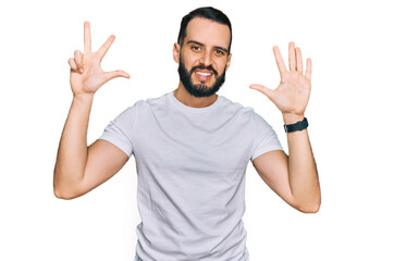 Young man with beard wearing casual white t shirt showing and pointing up with fingers number eight while smiling confident and happy.