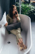 © undrey - Woman sits in the bathtub with her laptop and calls