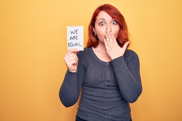 Wall Mural - Young beautiful redhead woman asking for equality holding paper with we are equal message covering mouth with hand, shocked and afraid for mistake. Surprised expression