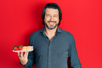 Canvas Print - Middle age caucasian man eating fresh and healthy fruit looking positive and happy standing and smiling with a confident smile showing teeth