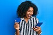 Beautiful african american woman with afro hair holding smartphone and credit card smiling and laughing hard out loud because funny crazy joke.