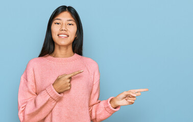 Beautiful young asian woman wearing casual winter sweater smiling and looking at the camera pointing with two hands and fingers to the side.