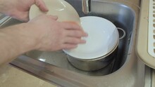 Man Washes Dishes In An Iron Sink. He Carefully Wipes The Plates With A Sponge. The Water In The Tap Is Turned Off. Close Up Shot