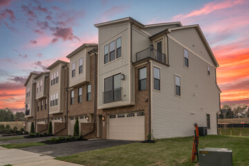 Wall Mural - Affordable Luxury 2-Car Garage Townhomes resort-style amenities, close to commuter routes. American real estate development neighborhood street dramatic orange, purple, red sunset sky background