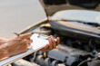 The auto mechanic checks the car engine with the check written in the car service engine repair checklist notebook.