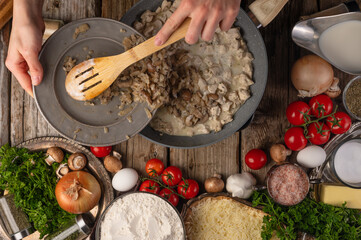Wall Mural - The chef fries chicken fillet with pieces with mushrooms in a frying pan, top view on a background with ingredients. Cooking & Recipe Book