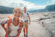 Hiking Couple Walking With Backpacks On Lava Field Trail In Hawaii. Summer Travel Happy Smiling Asian Girl And Man Hikers Outdoor Adventure On Big Island, USA.