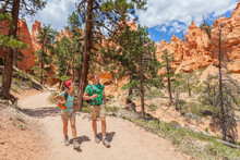 People Hiking - Couple Hikers In Bryce Canyon Walking On Trail Happy With Backpacks. Multiracial Young Asian Woman And Caucasian Man In Bryce Canyon National Park Landscape, Utah, United States.