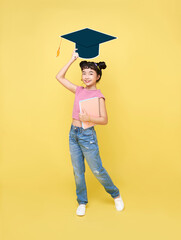 Wall Mural - Happy Asian cute schoolgirl with graduation hat and book isolated on yellow background.