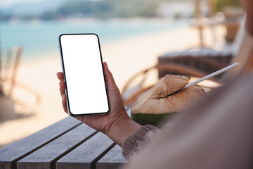 Mockup image of a woman holding mobile phone with blank desktop screen on the beach