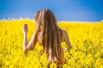 Wall Mural - Happy woman in field of rapeseed blooming in the summer. Girl enjoying sun in flowers of canola. Freedom concept.