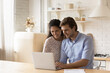© fizkes - Happy young couple using laptop in modern kitchen together, looking at screen, pleasant family surfing internet, wife and husband shopping or chatting online, browsing internet banking services