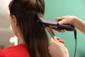 Wall Mural - Stylist straightening woman's hair with flat iron in salon