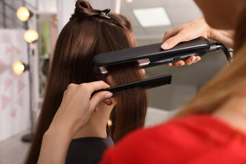 Stylist straightening woman's hair with flat iron in salon