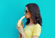 Portrait close up of young woman eating banana on a blue background