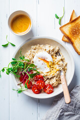 savory oatmeal with poached egg, tomatoes, cheese and sprouts in white bowl, top view. healthy break