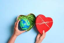 Female Hands Holding Heart Gift Box With Planet Earth On A Blue Background. Earth Day.