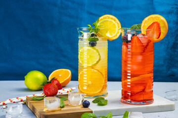 Two glasses of refreshing summer lemonade with ice. Cocktail with strawberry and lemon and cocktail with lemon and lime on the blue background