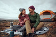 © StratfordProductions - Smiling young man and woman looking at each other with love and preparing morning drink at campsite during winter