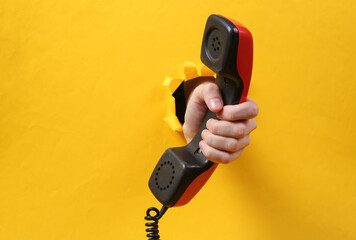 Wall Mural - Female hand holds telephone tube through torn hole yellow paper. Concept art. Minimalism