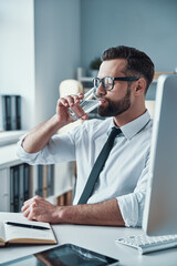 Canvas Print - Handsome young man in shirt and tie drinking water while sitting in the office