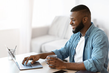 Wall Mural - Telecommuting Concept. Young Smiling Black Freelancer Guy Working On Laptop At Home