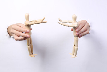 Canvas Print - Female hands holding wooden puppets through torn hole white paper. Puppeteer. Minimalism