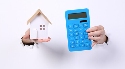 Wall Mural - Female hands holding house figure and calculator through torn hole white paper.