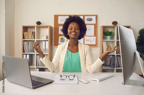 Obraz Dibond Happy employee getting ready to start productive work day. Young business woman sitting at office desk and meditating eyes closed thinking of good things and focusing on positive feelings and emotions
