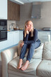 © shapovalphoto - woman blond hair using smartphone, sit on sofa at home, relax time