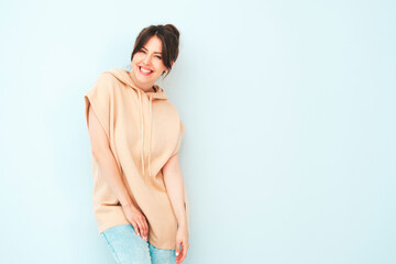 Wall Mural - Young beautiful smiling female in trendy summer hipster clothes. Sexy carefree woman posing near light blue wall in studio. Positive model having fun indoors. Cheerful and happy