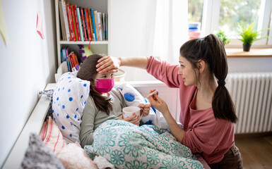 mother looking after sick small daughter in bed at home, coronavirus concept.