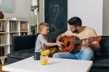 Wall Mural - father do playing acoustic guitar with his son. they are sitting in living room