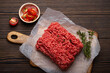 Fresh raw minced meat from ground beef or pork with ingredients for cooking on cutting board and dark brown rustic wooden background from above 
