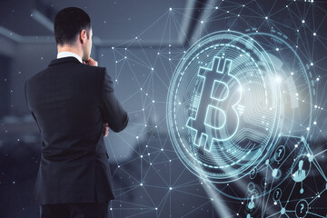 Wall Mural - Businessman in a suit thinking and faced forward, standing in an office with big windows, bitcoin logo. Cryptocurrency and trading concept