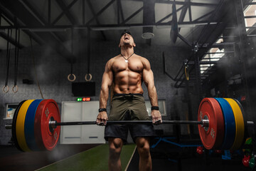 Weightlifter in the gym, a moment before a strong movement. Strong muscular man holds a heavy barbell in his hands and performs a dead lift in a gym with a dark atmosphere. Screaming during exercises