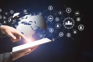 Aufkleber - Hand with a tablet holding and touching the globe icon with muptiple small application icons near it on a dark background. Worldwide web and social interaction concept