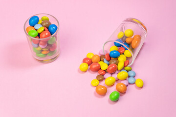 Multicolored chocolate candies scattered in two glass on pink background.Top view of creative colorful sweets background concept with copy space for text.