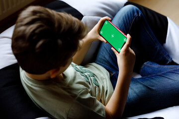 Kid boy gaming or using social media on mobile phone. chroma key compositing the hands of Internet. Child holding smartphone with green screen for commerce, new app and internet. With tracking points