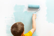 © Patryk Kosmider - Little boy is painting the walls of his room with a roller in turquoise color.