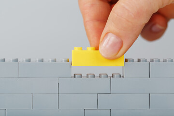 The hand puts the last yellow brick on the toy gray wall from the construction set.