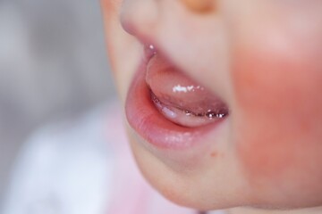 A close up portrait of a baby mouth with the first two small white teeth coming out of the gums below its tongue. The two teeth are only a few millimeters long and are visible in its smile.