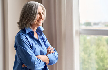 Wall Mural - mature happy laughing 60s middle aged business woman standing indoors in home office, arms crossed. 