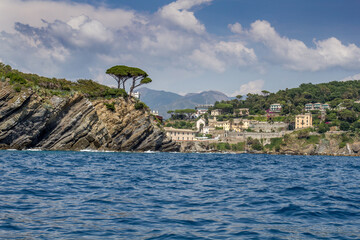 Seascape with azure water in the foreground and Italian port city and rocky coastline in the background