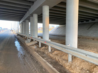 Construction industrial work under a bridge with columns and bumpers and a large car overpass road