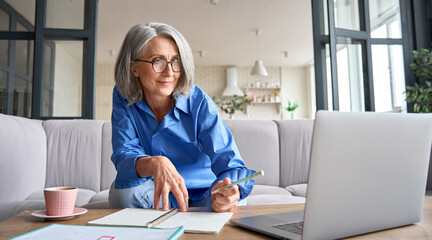 Senior mature older senior adult professional business woman working on laptop from home office, having virtual video call meeting, watching online training webinar e learning class using computer.